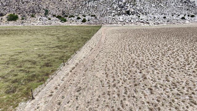 Aerial view of the Karoo landscape showing a fence line dividing green pasture from arid textured earth with rocky hills in the background, Beaufort West, Western Cape, South Africa.