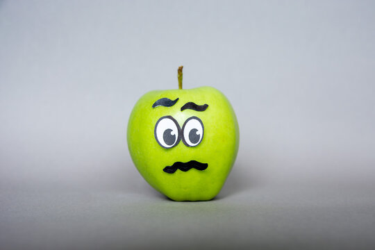 Funny green apple  Face  character with confused  expression on grey background. Abstract image of human emotions 