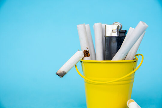 Cigarettes and lighter in a bucket on a blue background, stop smoking concept