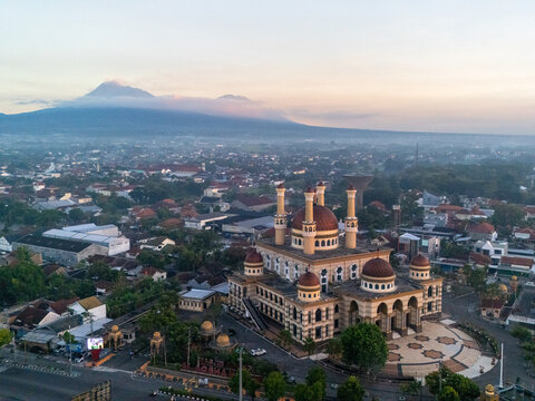 Aerial view of the Al-Aqsha Mosque with its distinctive domes surrounded by the urban landscape of Klaten and the majestic Mount Merapi in Klaten, Central Java, Indonesia.