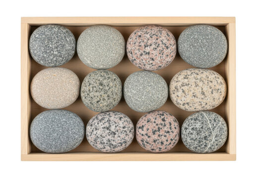 Twelve smooth, polished river stones of various granite textures and colors arranged in a neat grid inside a light-colored wooden rectangular box against a black background