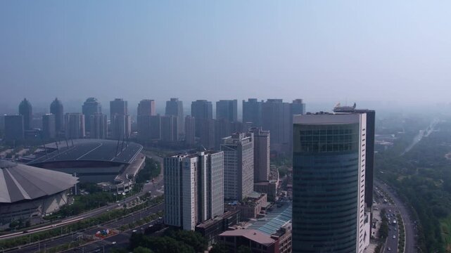 A hazy daytime view of an urban area featuring modern skyscrapers, a large stadium, and road networks.