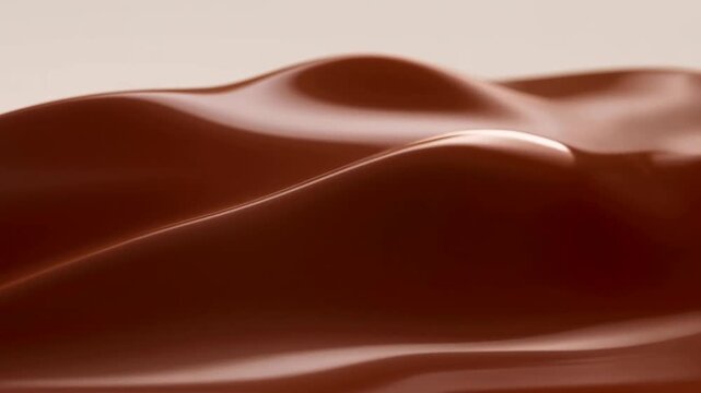 Slow tracking pan of chocolate liquid waves undulating and forming glossy ripples on tabletop studio close up