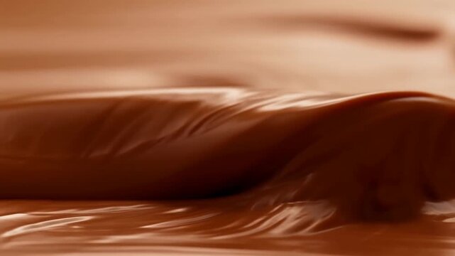 Slow motion close up tracking of melted chocolate flowing and folding across tabletop surface in studio kitchen setup