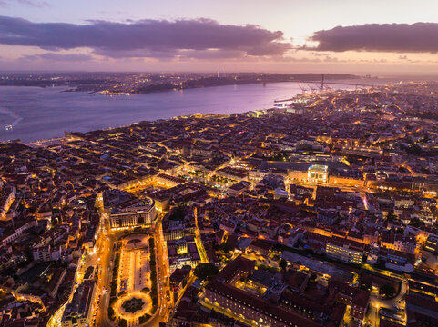 Aerial view of Lisbon at twilight, featuring the illuminated cityscape, historic rooftops, the Tagus River, and the 25 de Abril Bridge, Lisbon, Lisbon, Portugal.