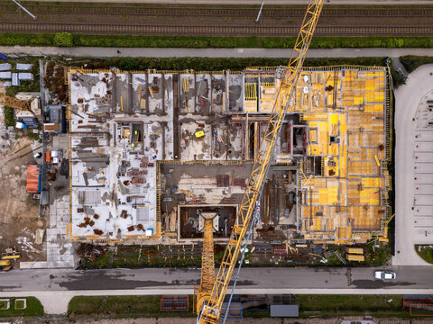 Aerial view of a construction site featuring a large yellow crane, concrete foundations, and steel reinforcement structures in Gdansk, Poland.