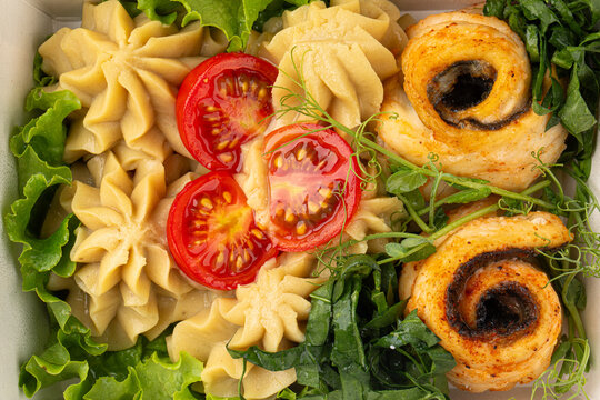 Healthy meal box with roasted fish rolls creamy mashed potatoes cherry tomatoes and fresh greens close up