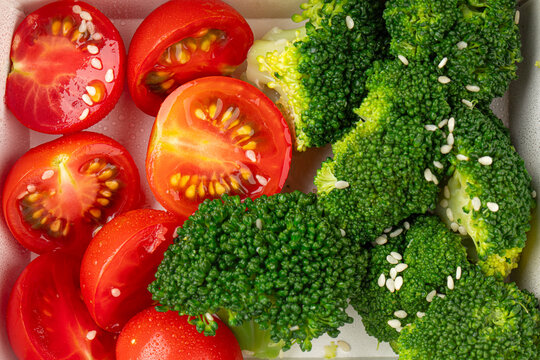 Fresh broccoli florets and juicy cherry tomato slices sprinkled with sesame seeds packed in a paper container box