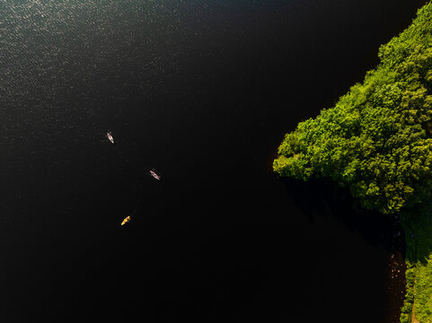 Aerial view of three kayaks paddling on the dark water of a lake near the lush green forest of Hale Reservation in Dover, Massachusetts, United States.