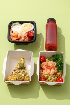 Takeaway meal boxes with prawn salad quiche slice zucchini noodles with shrimps and berry juice on green background