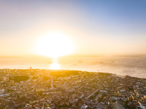 Aerial view of the cityscape of Lisbon at sunset with the Tagus River reflecting the golden light, historic buildings and rooftops visible in Lisbon, Lisbon, Portugal.