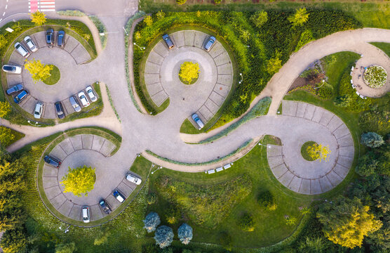 Aerial view of a circular parking lot with cars parked in a spiral pattern, surrounded by lush green trees and manicured landscaping in Sopot, Pomeranian Voivodeshi, Poland.
