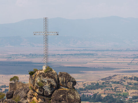 Aerial view of the large metal cross atop the rocky outcrop of Marko's Towers overlooking the vast rural landscape of Prilep, Prilep Municipality, North Macedonia.