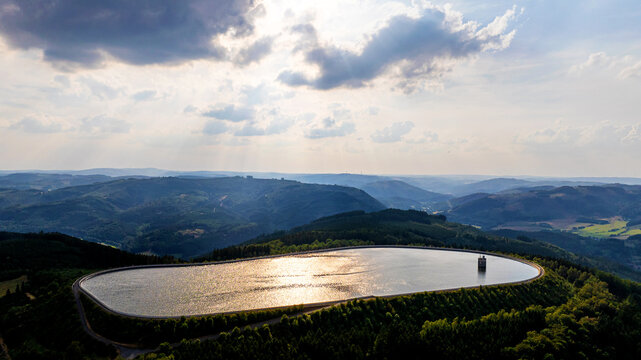 Aerial view of Pumpspeicherkraftwerk Ronkhausen, a reservoir surrounded by dense forests and rolling hills under a dramatic sky Finnentrop, Nordrhein-Westfalen, Germany.