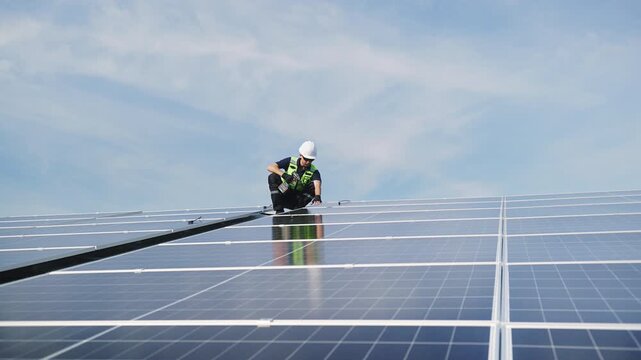 Technician installing solar panels on factory roof for green energy. A skilled technician in safety gear is working on a solar panel installation on rooftop. clean energy renewable power technology.