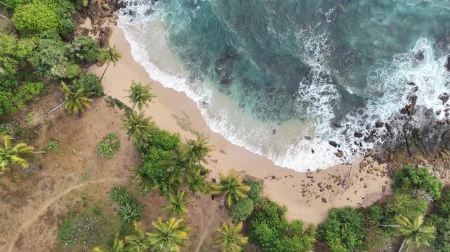 Aerial view of the tropical coastline at Silent Beach in Sri Lanka, with clear blue water, sandy beach, lush vegetation and secluded coastal scenery, 4k.