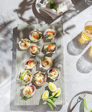 Baked scallops in shells with melted cheese and fresh lime on wooden board
