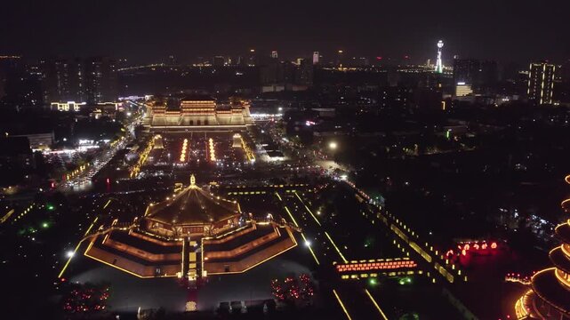 Aerial night shot of a grand traditional ancient architectural complex with illuminated structures and surrounding cityscape.