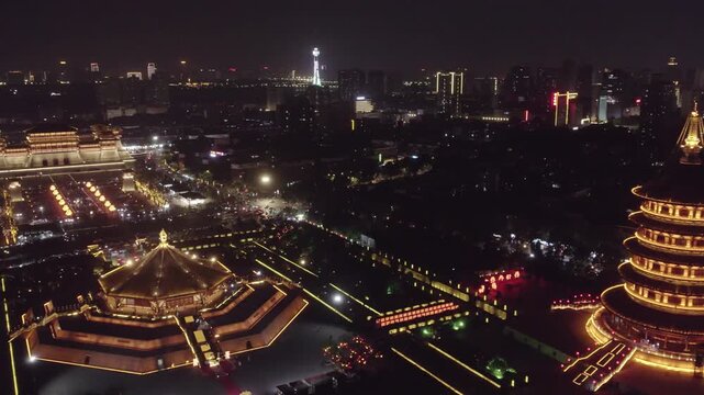 Aerial night view of an illuminated traditional architectural complex in a modern city, with historic structures and urban skyline.