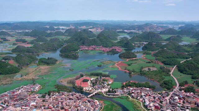 An aerial panorama shows karst hills, wetland lakes, and clustered rural settlements under a clear sky.