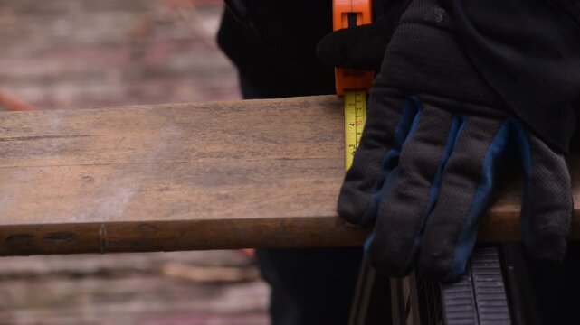 Close-up front view of a person using a tape measure to measure and mark a wooden board lengthwise, illustrating precision carpentry, woodworking, and DIY construction.