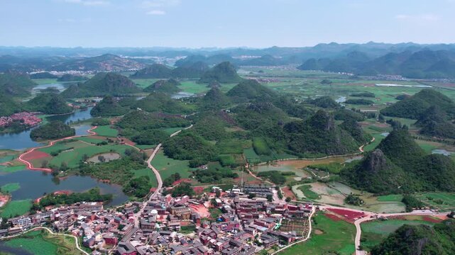 Aerial panorama of karst landform with rural settlements, farmlands and water bodies under clear sky.