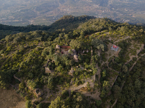 Aerial view of Tilla Jogian Archaeological Site, featuring ancient stone ruins nestled among dense green trees and rugged hills in Dina, Punjab, Pakistan.