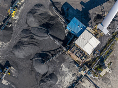 Aerial view of a coking plant facility with large piles of coal, conveyor belts, and industrial structures in Poland.