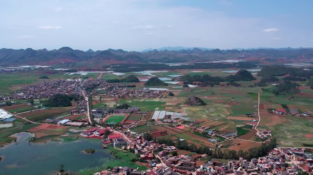 Aerial landscape of a rural settlement surrounded by karst hills, farmlands and water bodies under clear sky.