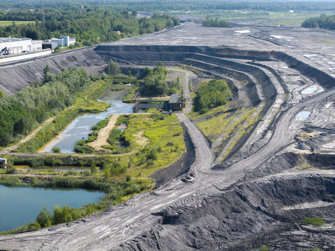 Aerial view of an industrial coking plant site with excavation pits, sediment ponds, and surrounding green forest in Poland.