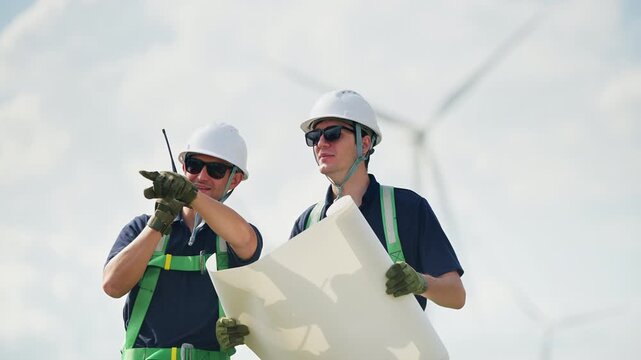 Engineers wearing safety helmets and jackets inspecting a wind turbine at wind farm at sunset. Concept renewable energy, sustainable technology wind power maintenance and environmental engineering.