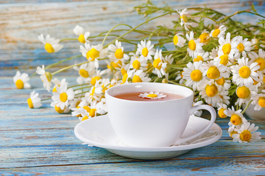 Daisy flowers in a white cup of tea, chamomile herbs on wooden background. Herbal medicine. Healthy lifestyle concept.