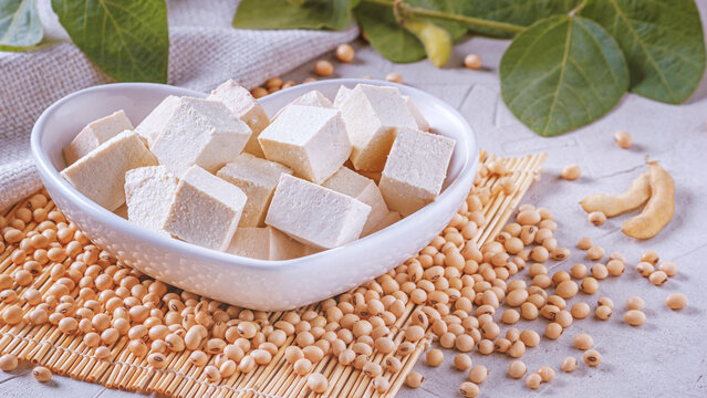 Tofu, also known as bean curd, diced in a faience white bowl in the form of heart on a bamboo napkin, closeup with selective focus