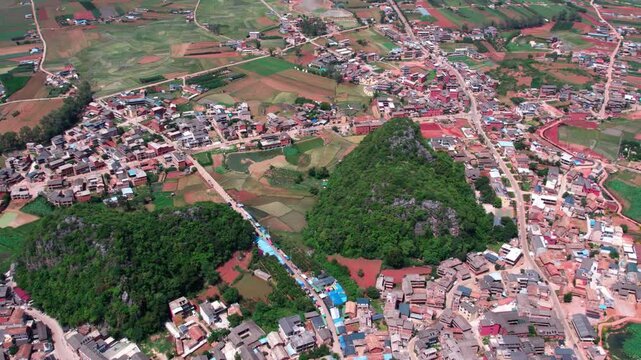 High-angle aerial shot of a rural settlement with buildings, green hills and surrounding farmland.