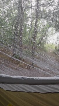 Raindrops trickle down the clear plastic window of a cozy camping tent pitched in a misty green forest. Concept of peaceful shelter, wilderness camping, and solitude in nature.