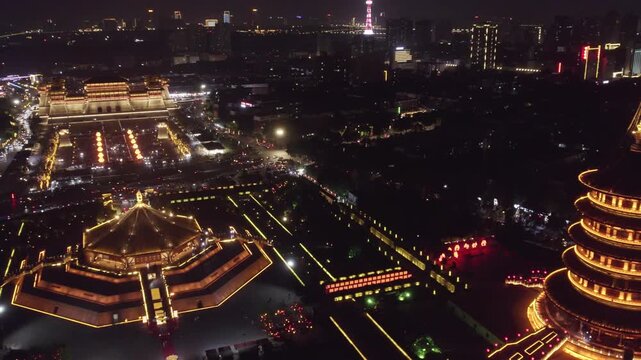 Aerial night view of illuminated traditional ancient architecture and modern urban buildings, showcasing cultural heritage and cityscape.