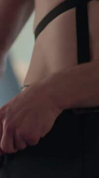 Close up of man with tattoos and sunglasses wearing strappy. Hands manipulate handcuffs near another man waist. Bright background suggests modern interior space with large windows