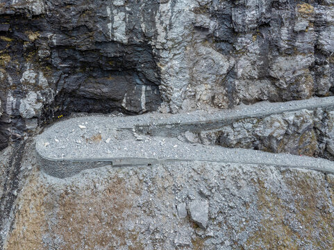 Aerial view of rockfall protection measures along the steep mountain cliffs of the Trollstigen road, featuring stone retaining walls and debris barriers in Andalsnes, More og Romsdal, Norway.