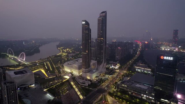 Twilight aerial view of modern twin skyscrapers and lit urban waterfront with river and roads.