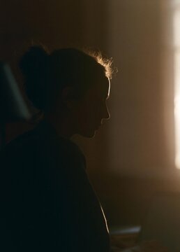Silhouette of a person sitting in front of a window. the person is facing away from the camera, with their head turned towards the right side of the image.