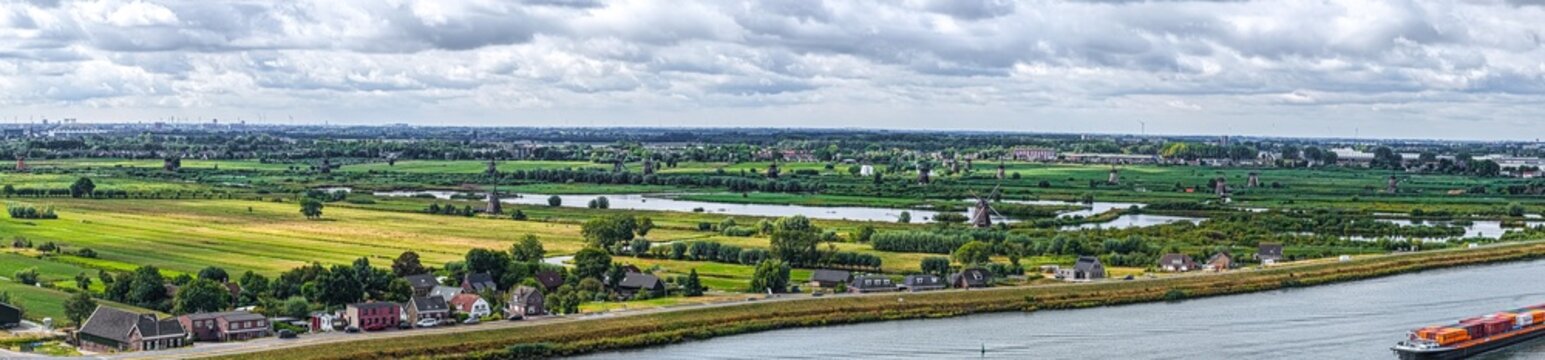 Aerial view of the historic UNESCO World Heritage Kinderdijk windmills set amidst lush green fields, winding canals, and a cargo ship in Kinderdijk, Zuid-Holland, Netherlands.
