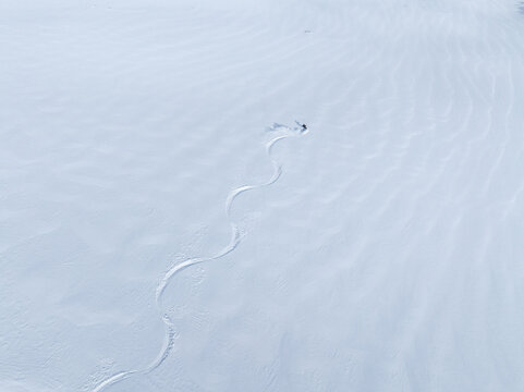 Aerial view of a lone skier carving a winding track through the pristine snow on the slopes of Ringshornet Fjord, More og Romsdal, Norway.