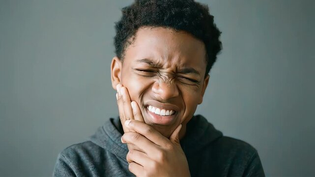 A young man holds his cheek with one hand, enduring severe tooth pain.
