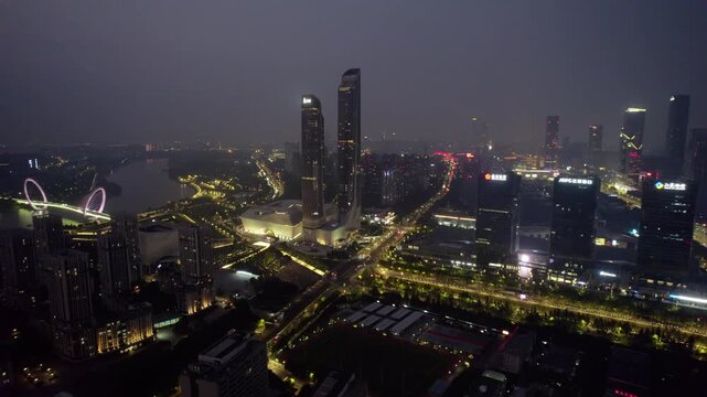 A nighttime aerial view of a modern urban area featuring twin high-rise towers, a river, illuminated roads and city buildings.