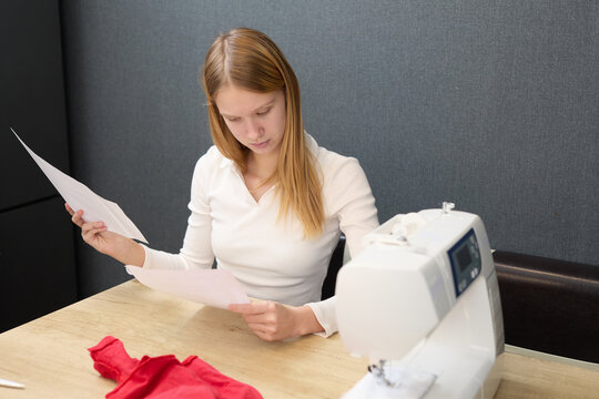 The young seamstress is using a sewing machine to create custom‑made clothing. The girl is studying the instructions.