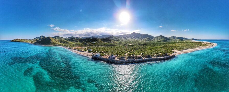 Aerial view of Parque Nacional Cabo Pulmo featuring turquoise waters, sandy coastline, and lush mountainous landscape under a bright sun in Cabo Pulmo, Baja California Sur, Mexico.