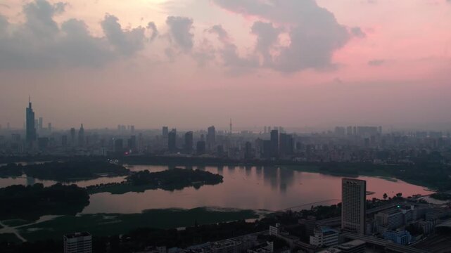 Aerial view of urban skyline reflected on a calm lake during dusky hour with cloudy sky in background.
