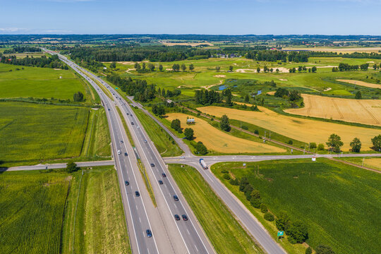 Aerial view of the Droga Ekspresowa S7 expressway cutting through lush green agricultural fields and rural landscape in Paslek, Warmian-Masurian Voivodeship, Poland.