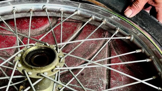A close-up of a person's hand holding a heavily damaged bicycle tire with a large tear or hole in the sidewall. Showing a flat tire needing repair or replacement on a concrete ground.