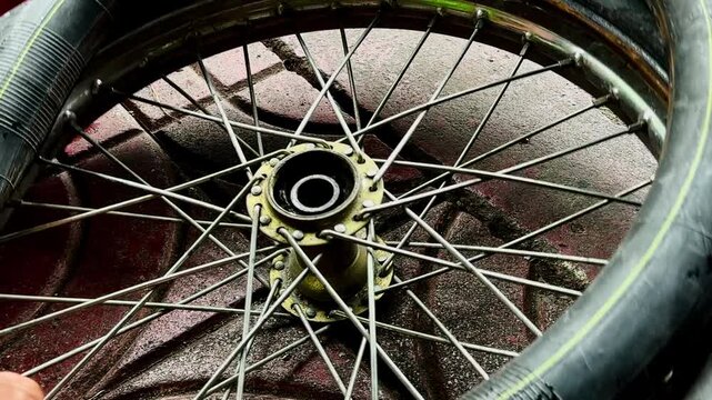 A close-up of a person's hand holding a heavily damaged bicycle tire with a large tear or hole in the sidewall. Showing a flat tire needing repair or replacement on a concrete ground.